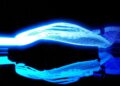 Bright blue neon light trails and reflections appear against a black background, forming abstract, wave-like patterns—reminiscent of the speed and innovation as Two Fords EVs, Lightning SuperTruck and SuperVan, conquer the Green Hell.