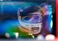 A race car driver wearing a white Ford helmet looks through a car window, with colorful reflections on the glass—channeling the spirit of Two Fords EVs, Lightning SuperTruck and SuperVan, as they conquer the Green Hell.