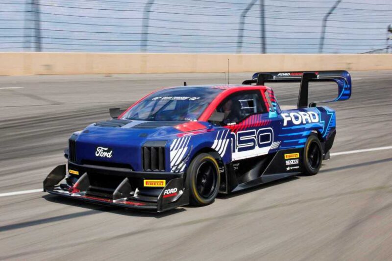 A blue and red Ford electric race truck with aerodynamic body modifications drives on a racetrack, as Two Fords EVs—Lightning SuperTruck and SuperVan—conquer the Green Hell, breaking two records.