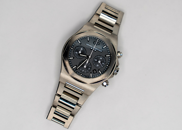 A stainless steel Girard-Perregaux wristwatch with a black chronograph dial and metal bracelet, photographed on a plain white background—a true reflection of Time Well Spent.