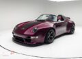 A maroon Porsche Gunther Werks Speedster convertible with black racing stripes is displayed in a white studio setting.