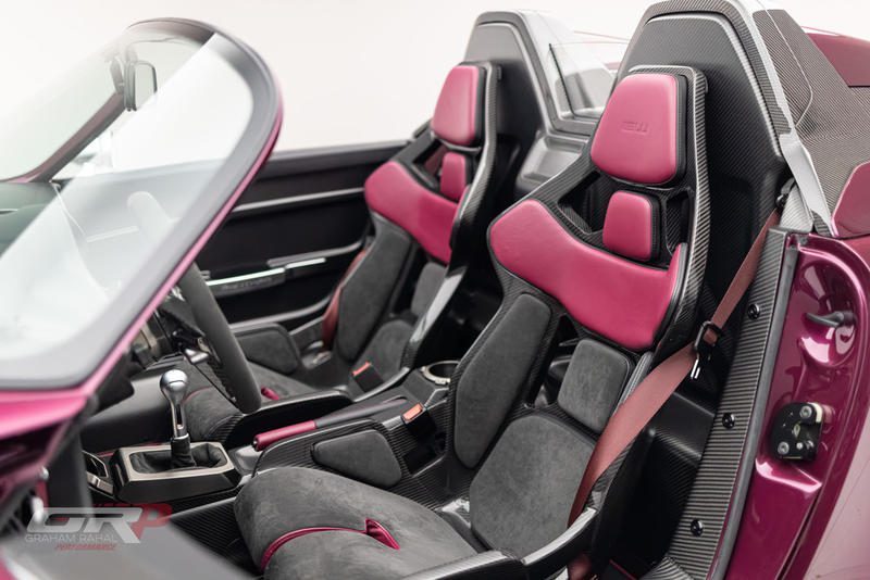Close-up view of a luxury car's interior featuring two-tone black and magenta racing seats, carbon fiber accents, and a manual gear shifter—exemplifying the unique craftsmanship of the Gunther Werks Speedster.