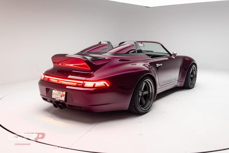 A maroon Gunther Werks Speedster with black wheels and a rear spoiler is parked in a white studio, its taillights illuminated—an exceptional example of performance engineering by Graham Rahal Performance.