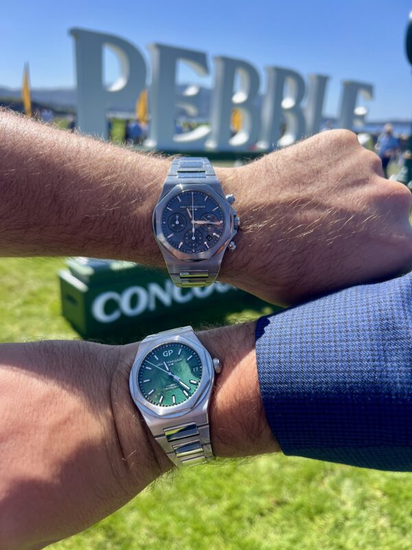 Two people display luxury wristwatches on their wrists outdoors at Monterey Car Week, with blurred "PEBBLE" and "CONCOURS" signage visible in the background—a moment of Time Well Spent.