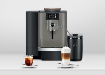A modern espresso machine with a milk frother, perfect for any office barista, accompanied by a glass of iced coffee and a glass of layered latte on saucers.