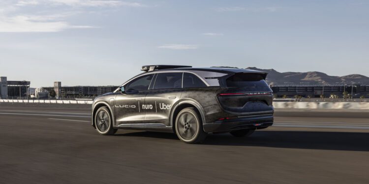 A black SUV with logos including Lucid, Nuro, and Uber drives on a highway, with city buildings and mountains in the background.