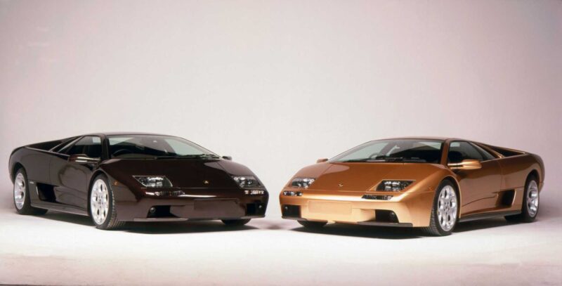 Two Lamborghini Diablo sports cars, one dark brown and one bronze, sit side by side on a plain white background—timeless icons as the Lamborghini Diablo turns 35: the last old-school analog Raging Bull still roars.