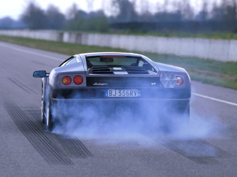 A Lamborghini Diablo VT accelerates on a road, producing tire smoke and leaving skid marks—proof that even as the Lamborghini Diablo turns 35, the last old-school analog raging bull still roars.