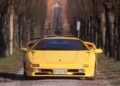 A yellow Lamborghini Diablo, the last old-school analog Raging Bull, is parked on a tree-lined driveway with a building and gated entrance visible in the background as the iconic supercar turns 35.
