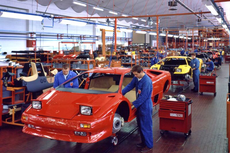 Workers assemble Lamborghini Countach sports cars on an automotive production line inside a brightly lit factory, as the legacy of the Lamborghini Diablo Turns 35: The Last Old-School Analog Raging Bull Still Roars inspires their craftsmanship.