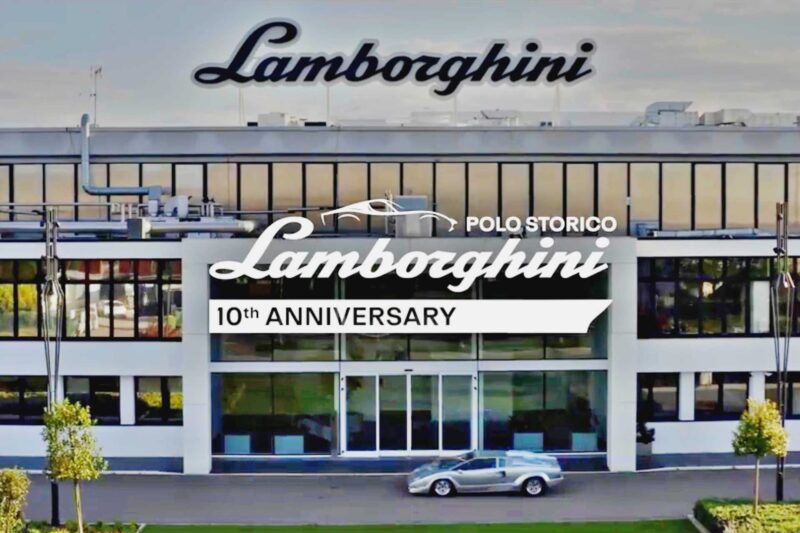 A silver Lamborghini is parked in front of a modern glass building with Lamborghini signage, celebrating the Polo Storico 10th Anniversary—a true tribute to Heritage Films and the brand’s storied legacy.