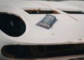 A sanding block rests on the hood of a white Lamborghini undergoing bodywork, with some areas showing exposed primer or filler.