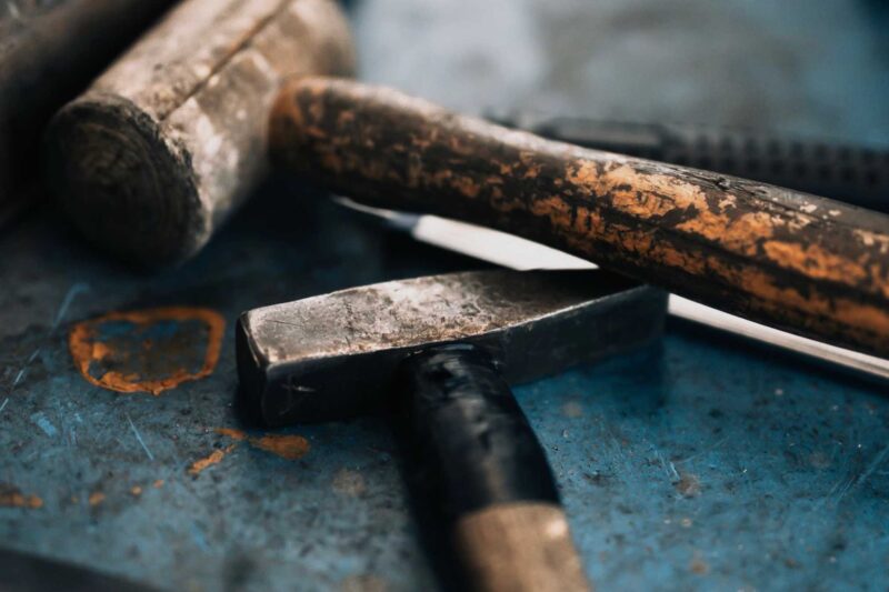 Close-up of worn hammers and a utility knife resting on a scratched, blue metal surface—tools reminiscent of those used in Lamborghini Polo Storico Heritage Films restorations.