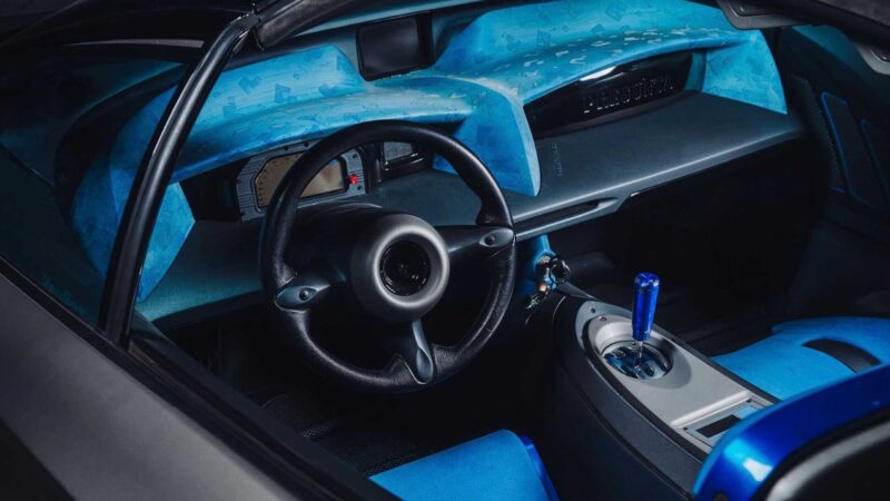 Close-up view of a car interior featuring a black steering wheel, blue dashboard, manual gear shift, and blue seats with minimalist, futuristic design elements—echoing the exclusive style of the 1-of-1 Lamborghini Pregunta.