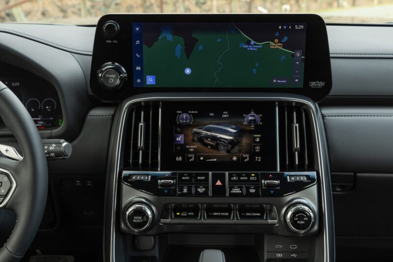 Car dashboard from the 2025 Lexus LX 700h Overtrail 4WD showing a large digital display with navigation map and a lower touchscreen for vehicle control settings, climate controls, and driving mode options—highly capable yet moderately practical.