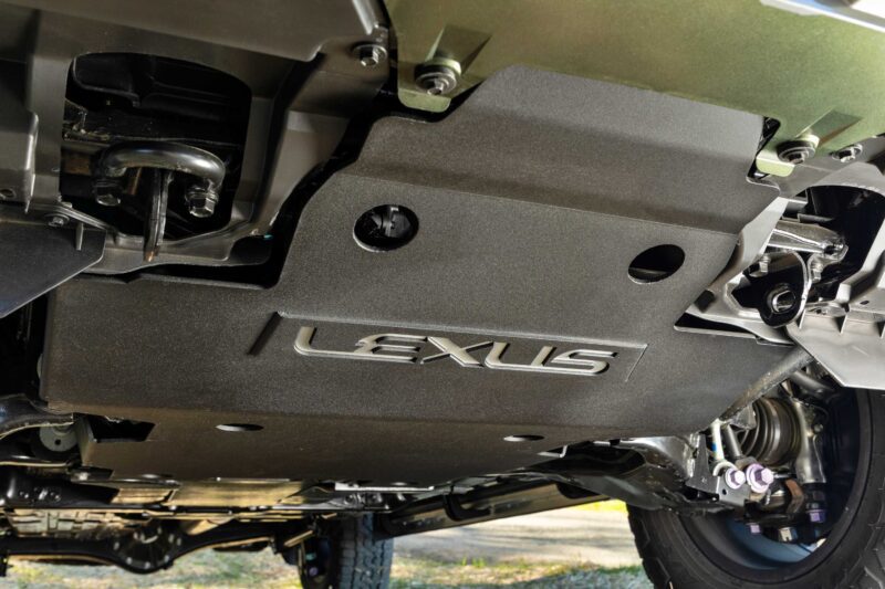 Close-up view of the underside of a vehicle, showing a protective skid plate with the Lexus logo—highlighting how the 2025 Lexus LX 700h Overtrail 4WD from our review is highly capable yet moderately practical. Bolts and suspension components are visible.