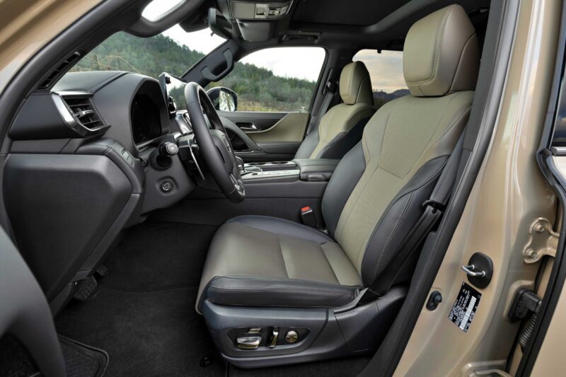 Front interior view of the 2025 Lexus LX 700h Overtrail 4WD, highlighting its driver and passenger seats, dashboard, steering wheel, and center console in a neutral color scheme. Review: Highly capable yet moderately practical design.