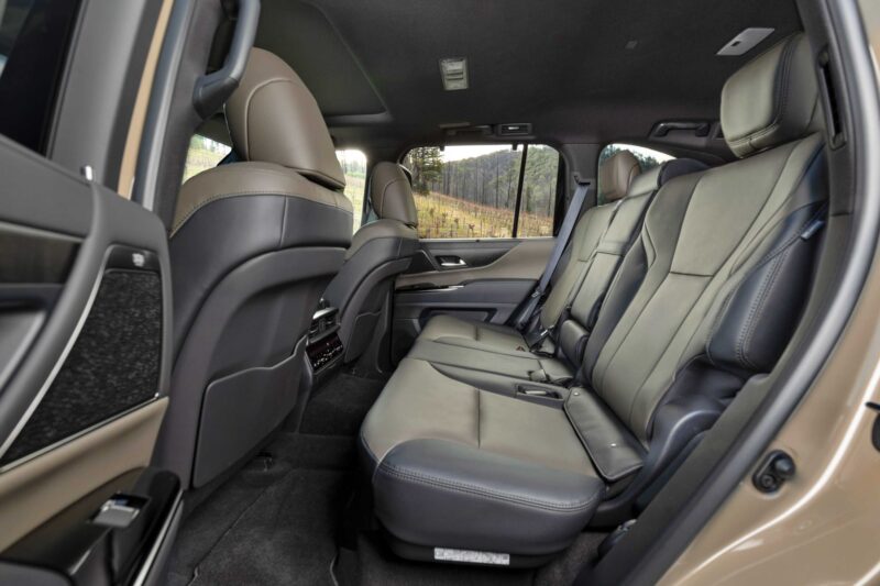 The interior of an SUV, as seen in the Review: 2025 Lexus LX 700h Overtrail 4WD Is Highly Capable Moderately Practical, showcases rear passenger seats in beige leather with seatbelts, armrest, and a clear view toward the front seats and dashboard.