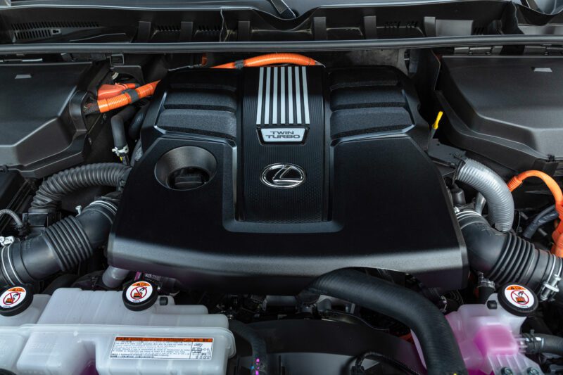 Close-up view of a Lexus engine bay featuring a black cover labeled "Twin Turbo," with visible orange electrical wires—highlighting the advanced engineering in the 2025 Lexus LX 700h Overtrail 4WD, as noted in our review for being highly capable and moderately practical.