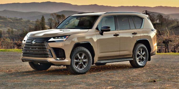 A beige Lexus SUV, the 2025 Lexus LX 700h Overtrail 4WD, is parked on dirt ground with mountains and trees in the background at sunset—showcasing its highly capable yet moderately practical design.
