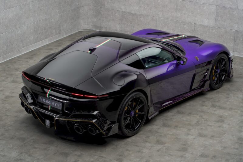 A black and purple luxury sports car with a carbon fiber finish, inspired by the MANSORY Previews Ferrari 12Cilindri-based Equestre, is parked in a tiled showroom with gray walls and flooring.