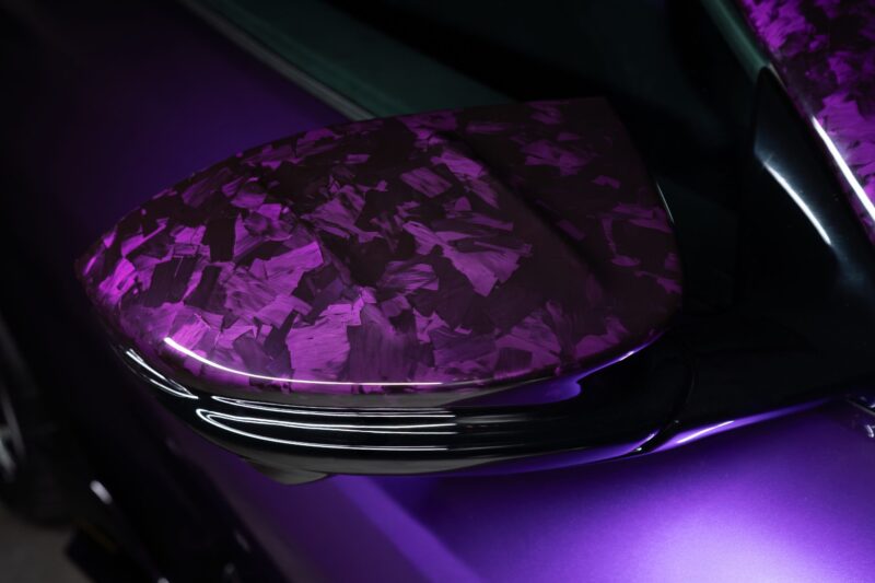 Close-up view of a car’s side mirror featuring a glossy, purple-patterned finish and a matching purple body, inspired by the MANSORY Previews Ferrari 12Cilindri-based Equestre ahead of the Monaco Yacht Show.