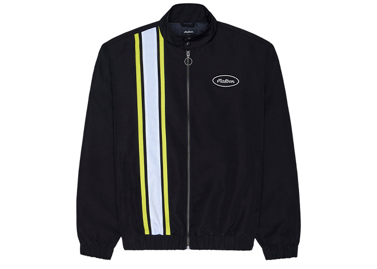 A black zip-up jacket from the Malbon Golf Capsule Collection, featuring yellow and white vertical stripes on the left side and a small oval “Pleasures” logo on the right chest.