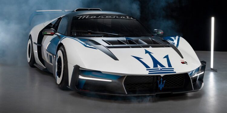 A white and black Maserati race car with blue accents and the Maserati trident logo on the hood, displayed indoors with smoke in the background.