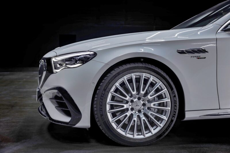 Close-up of the front left side of a white luxury sedan, showing the wheel, tire, headlight, and part of the grille with "Turbo" badging—reminiscent of details seen as Mercedes-AMG reveals pricing for the new E 53 HYBRID Wagon.