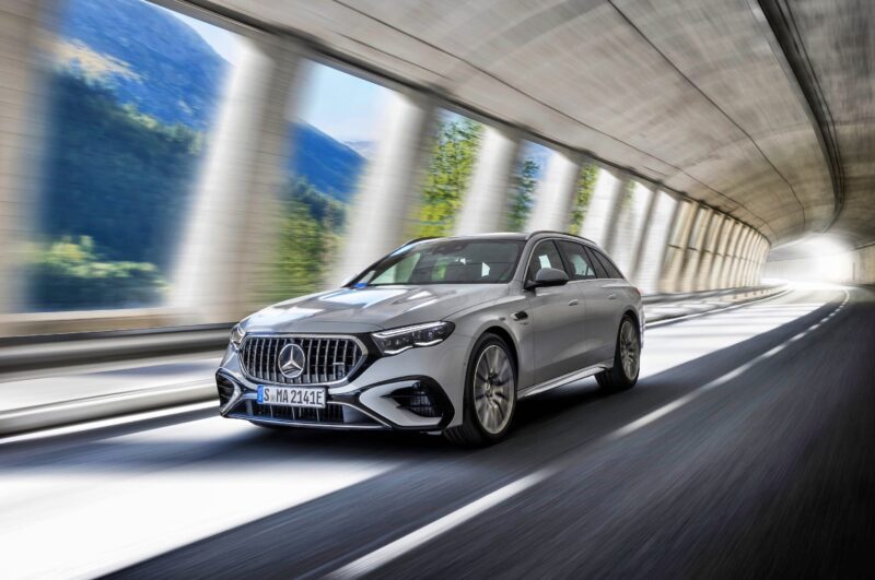A silver Mercedes-Benz station wagon, possibly the new E 53 HYBRID Wagon for which Mercedes-AMG reveals pricing, drives through a sunlit tunnel with blurred scenery in the background, suggesting motion.