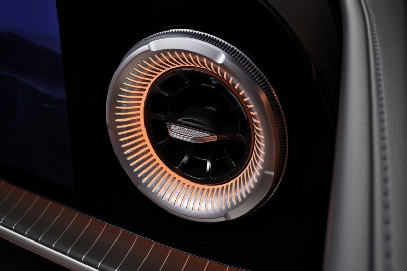 Close-up of a circular car air vent with illuminated orange accents, showing detailed metallic and black design elements within the modern interior of a Mercedes electric GLC.
