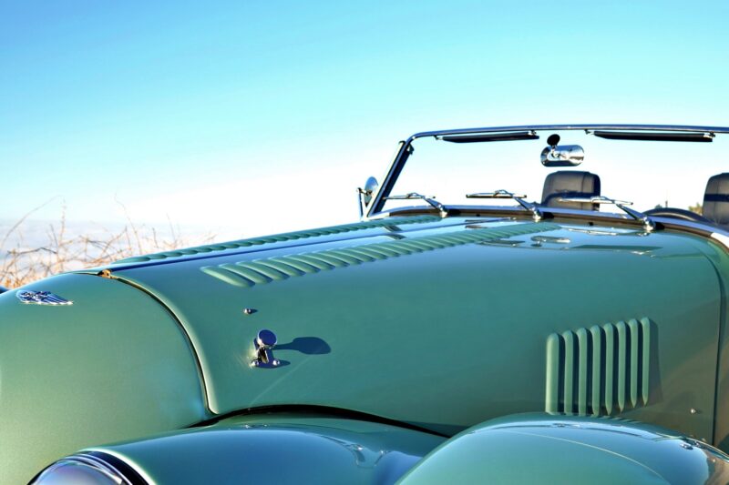 Green vintage convertible car with an open top, photographed from the front side against a clear blue sky—this scene evokes the spirit of the 2025 Morgan Plus Four Review: A Timeless Reminder of Olde-School Driving Fun.