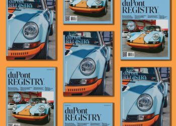 Several copies of the October 2025 duPont REGISTRY magazine, featuring a blue and orange vintage Porsche on the cover, are arranged on an orange background.