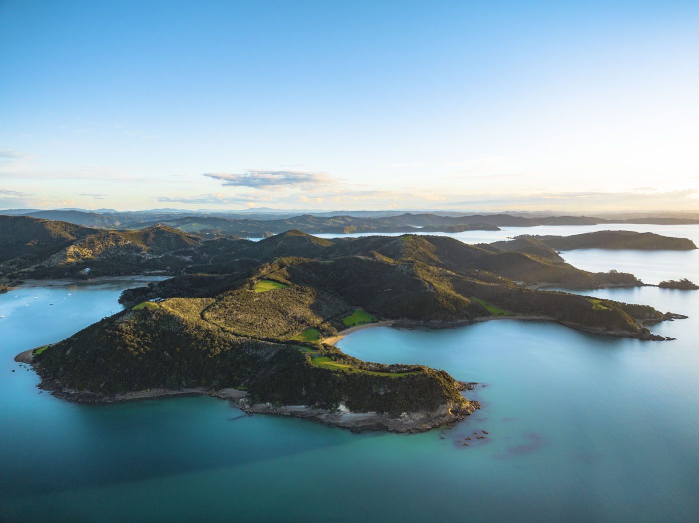 A coveted coastline unfolds in this scene—a large, green island surrounded by calm blue water under a clear sky at sunset.