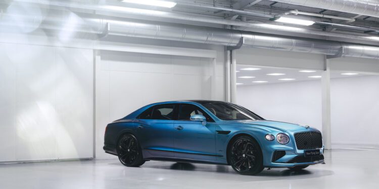 A blue luxury sedan with black wheels is parked in a brightly lit, modern industrial garage with white floors and walls.
