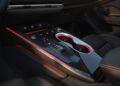 Close-up view of a modern 2026 Audi A6 center console featuring cup holders, control buttons, a gear selector, and ambient red lighting.