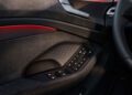 Close-up of a 2026 Audi A6 door interior featuring a geometric pattern, black trim, window and mirror control buttons, and red ambient lighting.