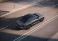 Aerial view of a gray 2026 Audi A6 luxury sedan, priced from $64,100, driving on an empty city street in daylight.