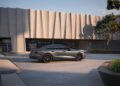 A sleek, dark gray 2026 Audi A6 sedan is parked in front of a modern building with wavy concrete panels and large windows on a clear day.