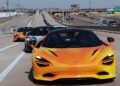 Three McLaren sports cars, led by an orange model, drive in a line on a multi-lane highway under clear skies, capturing the thrill of a States of Endurance road trip.