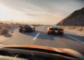 Two sports cars, including a McLaren, speed side by side on a desert highway during daylight, captured from behind another car in motion—a true States of Endurance road trip scene.