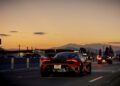 New Video: An orange McLaren sports car driving on a highway at sunset, with mountains and city buildings in the background, captures the thrill of an endurance road trip.