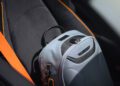 A gray backpack with black accents rests on a car seat with orange seat belts, ready for a road trip in a McLaren—embodying the spirit of States of Endurance.