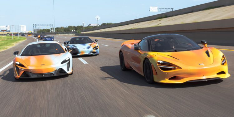 Three orange McLaren sports cars drive side by side on a multi-lane highway under a clear sky, embodying the spirit of a States of Endurance road trip.