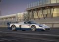 A record-breaking white and blue Maserati MC12 sports car is parked on a racetrack near a modern glass-fronted building at dusk, reminiscent of moments from its legendary MC12 auction appearances.