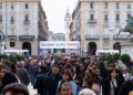 A large crowd gathers at an outdoor event in Turin, Italy, with a "Salone Auto Torino" banner signaling the excitement of the Turin Auto Show amid historic buildings.