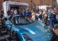 A blue Maserati sports car is on display outdoors at the Turin Auto Show, surrounded by a crowd near a Maserati booth and historical buildings.