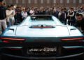 A crowd gathers around a light blue Maserati MC20 Cielo sports car, viewed from the rear, during the Turin Auto Show.