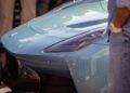 Close-up of a light blue Maserati sports car’s front hood and headlight, with a person in a denim outfit standing nearby at the Turin Auto Show.