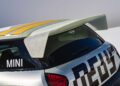 Rear view of a MINI car with a large rear spoiler, yellow and gray stripes on the roof, and geometric graphics—showcasing how MINI’s Rally DNA gets a Deus makeover in these two radical JCW builds.